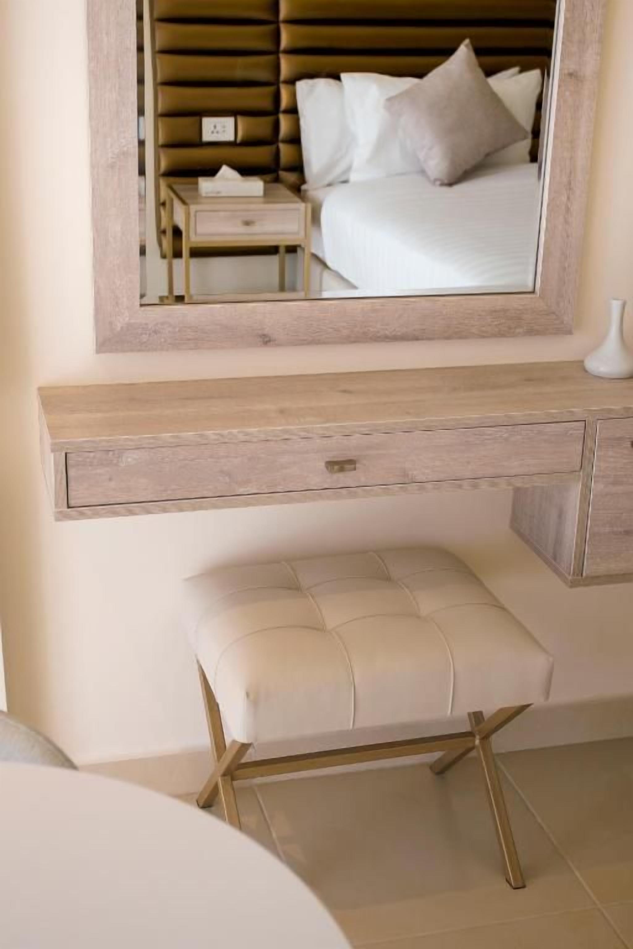 A bedroom with a bed, bedside table, nightstand, and a mirror above a wooden bench.