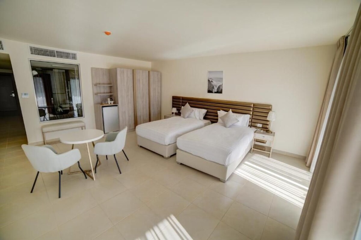 Habitación de hotel con cama doble, escritorio con silla, kitchenette pequeña y vista al exterior.