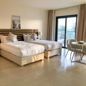 Habitación de hotel con dos camas, una silla, una mesa y un ventanal grande.