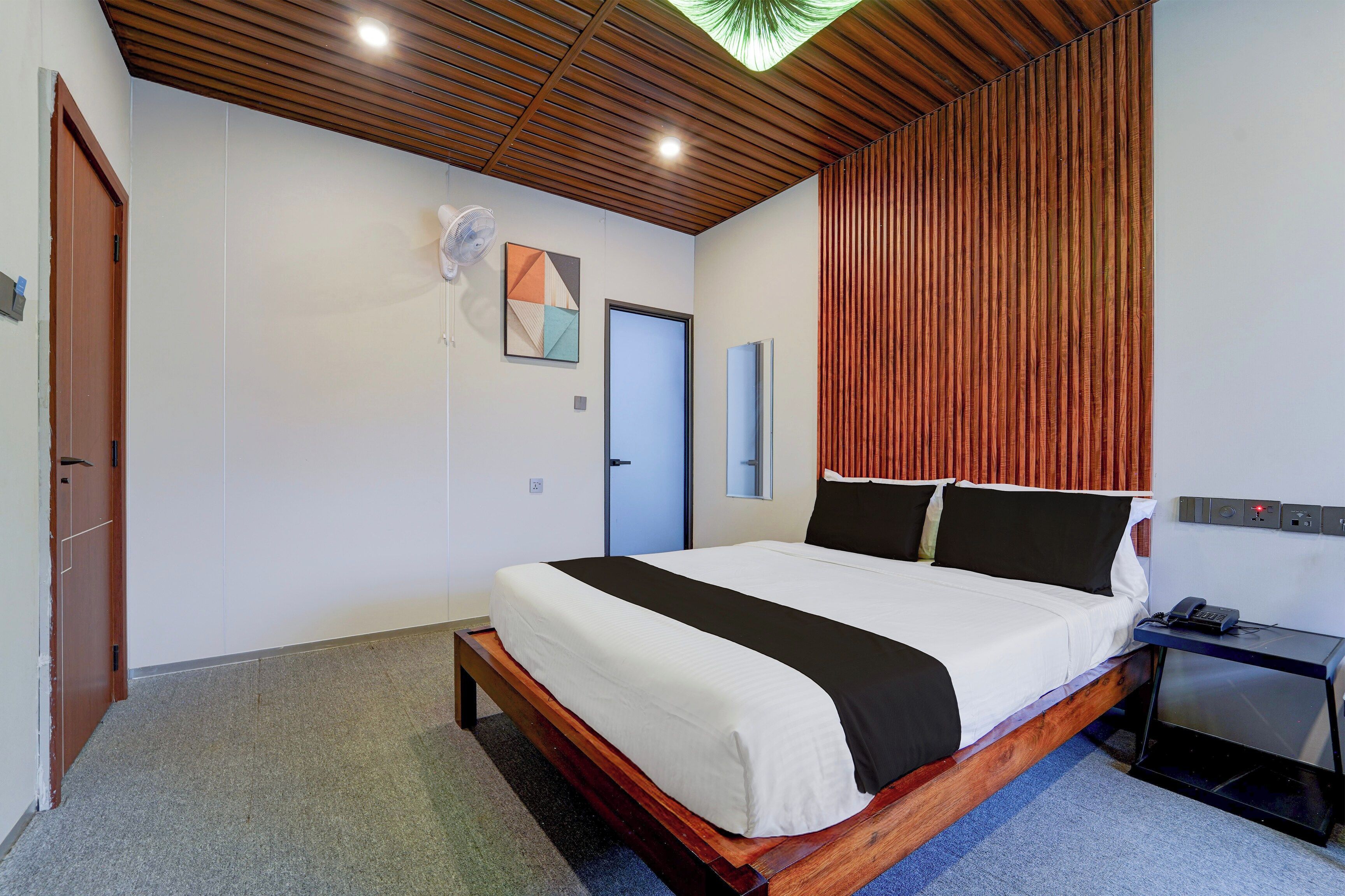 A modern bedroom with a wooden bed frame, a flat-screen TV, and a desk with a phone.