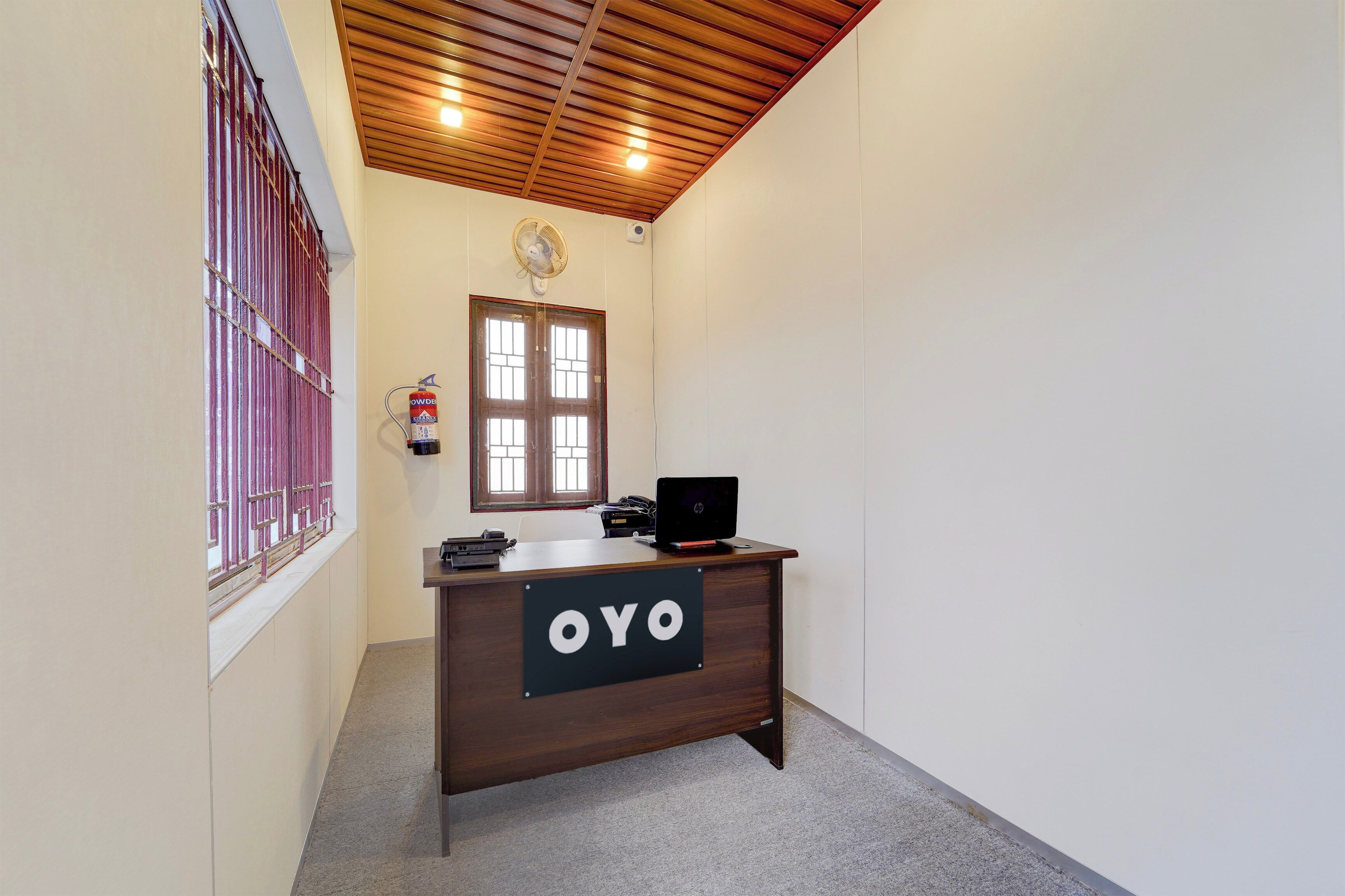 A reception desk with a sign that reads 'OYO' in a hallway with a wooden ceiling and a window with bars.