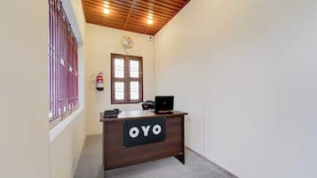 A reception desk with a sign that reads 'OYO' in a hallway with a wooden ceiling and a window with bars.