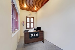 A reception desk with a sign that reads 'OYO' in a hallway with a wooden ceiling and a window with bars. - Hotel O AM Grandd (Karaikudi)
