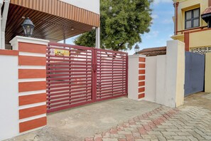 Una entrada protegida por un portón rojo, un muro de ladrillo y un área pavimentada que conduce a un edificio con techo de tejas.