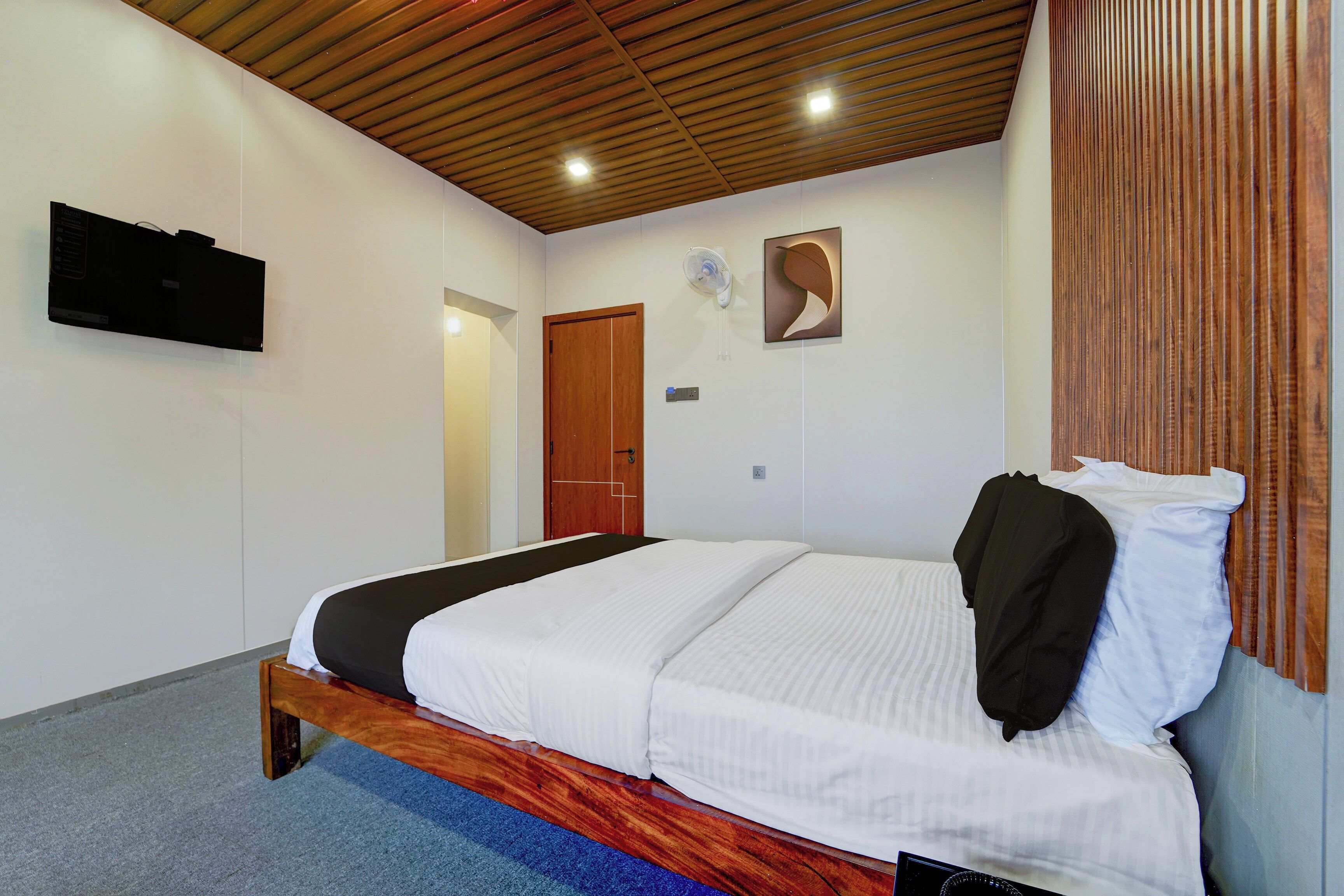 A bedroom with a bed, a wooden ceiling, a wall-mounted TV, and a door.