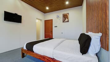 A bedroom with a bed, a wooden ceiling, a wall-mounted TV, and a door.