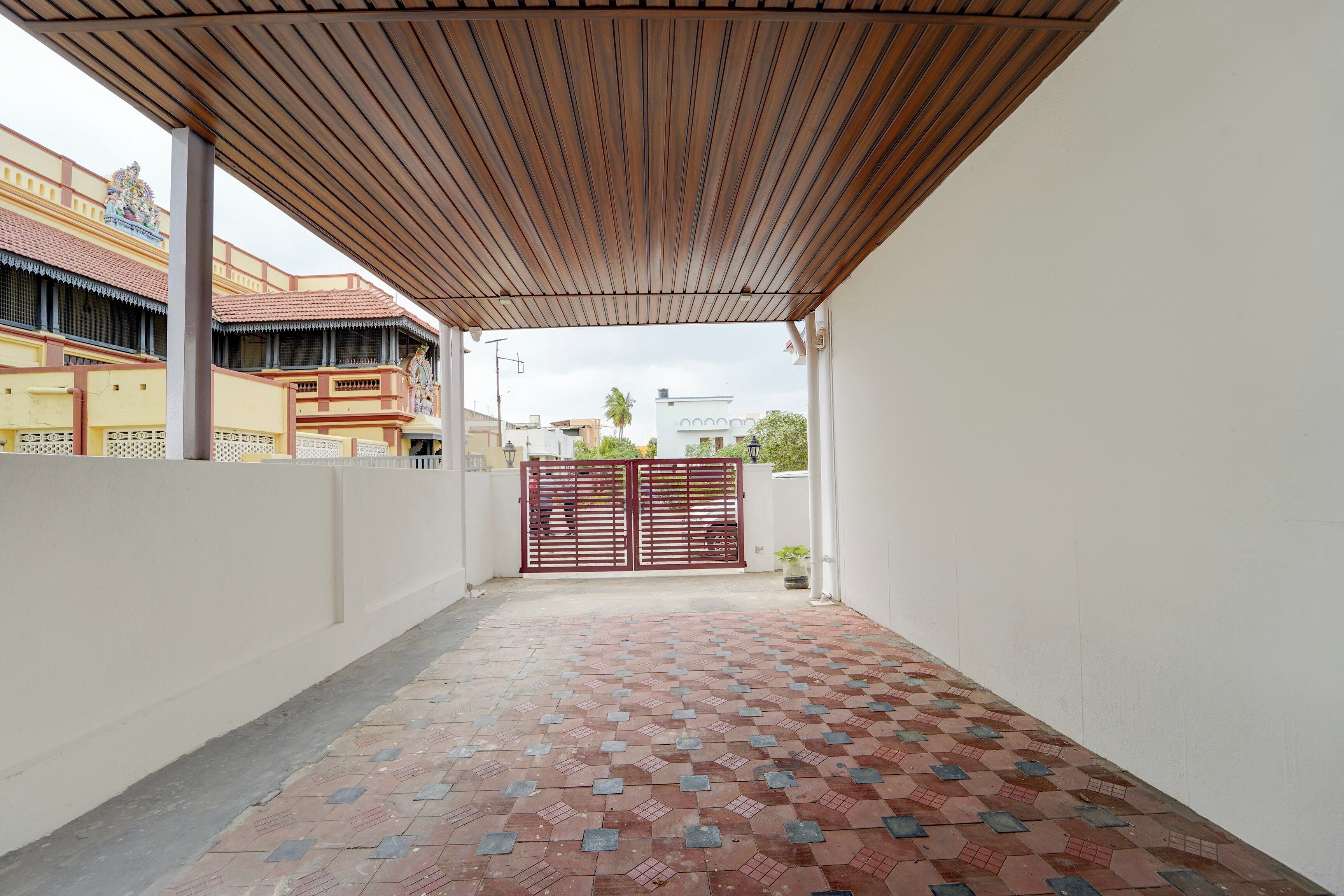 A covered outdoor area with a tiled floor, a gate, and a building in the background.