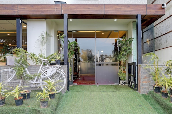 A building entrance with a bicycle parked outside, surrounded by potted plants. - Palette Hotel and Resort Manyata Tech (Bengaluru)