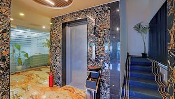 Un lobby moderno con piso de mármol, una escalera y una puerta con un teléfono.