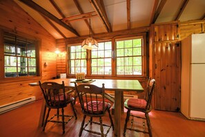 A wooden interior with a dining table, chairs, and a hanging light fixture. - New for 2026! Two Cottages on Sebago Lake w/ 160’ of Shoreline & Sunset Views (Naples)
