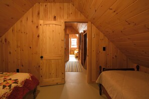 Ett rum med träpanel på väggarna, två sängar, en dörr som leder till ett annat rum och ett fönster som syns.