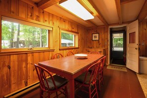 Ein Holzinterieur mit einem Esstisch und Stühlen, einem Fenster mit Blick auf Bäume und einer Tür, die nach draußen führt.