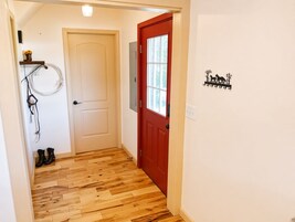 Un pasillo con piso de madera, una puerta roja y un adorno en la pared.