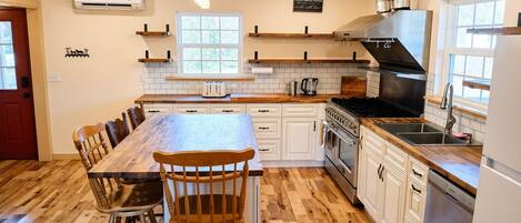 A kitchen with a central island, wooden chairs, white cabinetry, a stainless steel range hood, and a built-in oven.