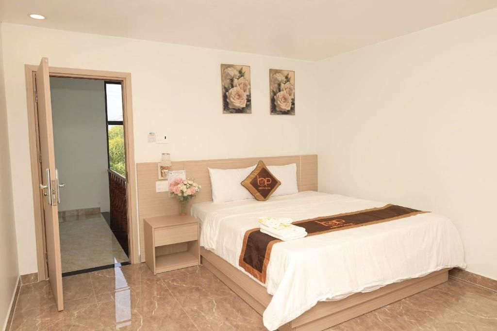 Una habitación de hotel con una cama, una mesita de noche, una pequeña mesa con un florero y dos cuadros en la pared.