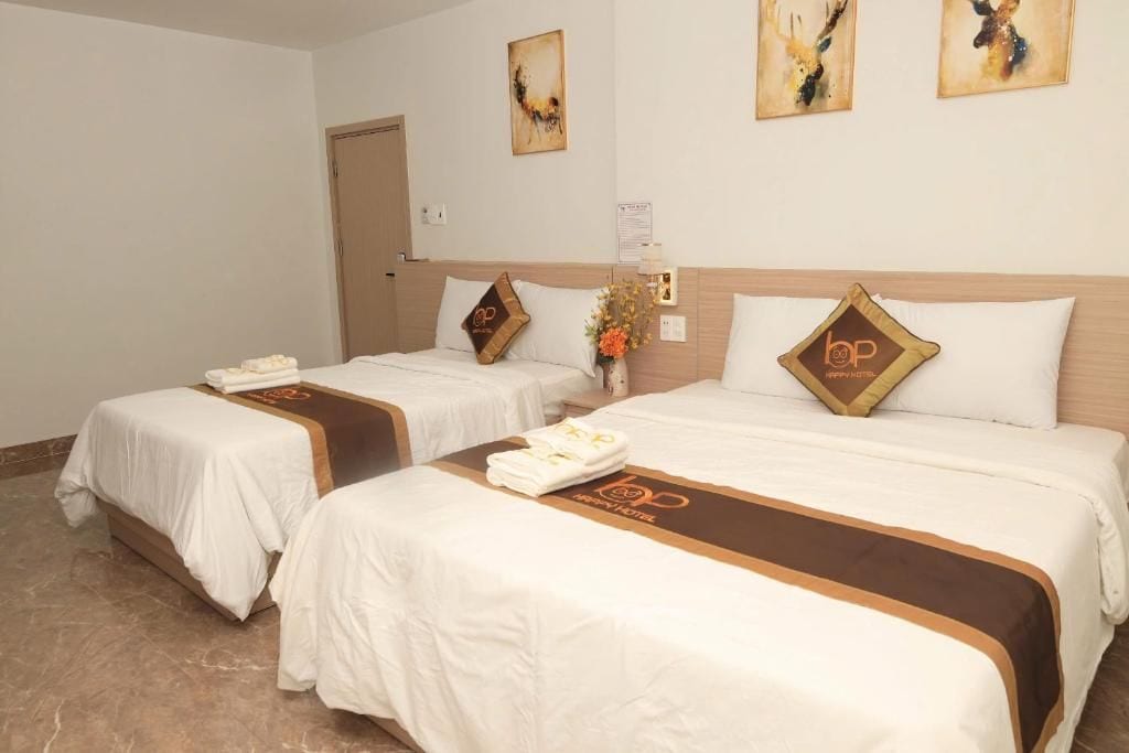 A hotel room with two beds, each with a brown headboard and a white bedspread. There are towels and a small vase with flowers on the beds.