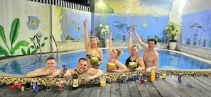 Um grupo de pessoas em uma piscina com um mural tropical na parede.