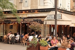 Een terras met tafels en stoelen, een bord met 'Cafe Restaurant' en een straatnaambordje voor 'Avenue Emile Zola'.