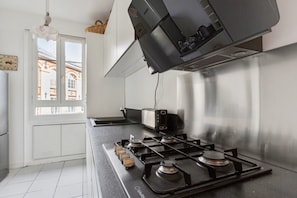 A modern kitchen with a gas stove, a toaster, and a window with a view of buildings. - A TRUE PARISIAN TREAT WITH PVT BALCONY & CAFE'S ALL AROUND (Paris)