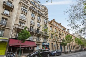 A multi-story building with balconies, a storefront with a red awning, and parked cars on the street. - A TRUE PARISIAN TREAT WITH PVT BALCONY & CAFE'S ALL AROUND (Paris)