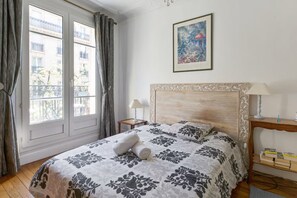 Een hotelkamer met een bed, nachtkastje, lamp, schilderij aan de muur en uitzicht door het raam.