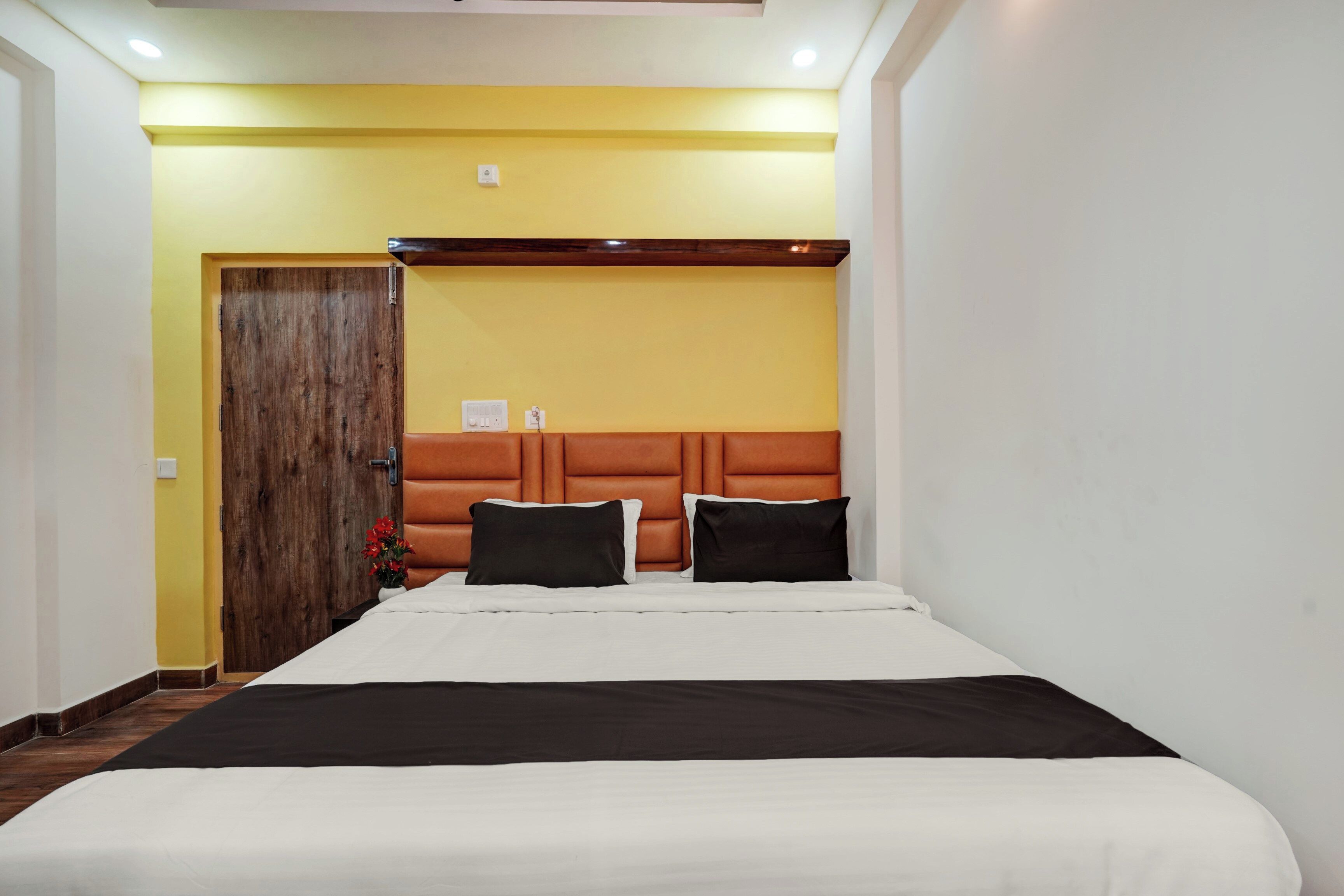 A hotel room with a bed, a wooden door, and a wall-mounted light fixture.
