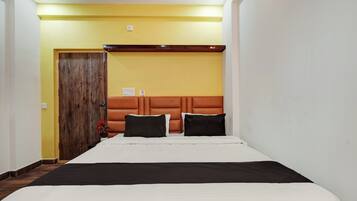 A hotel room with a bed, a wooden door, and a wall-mounted light fixture.