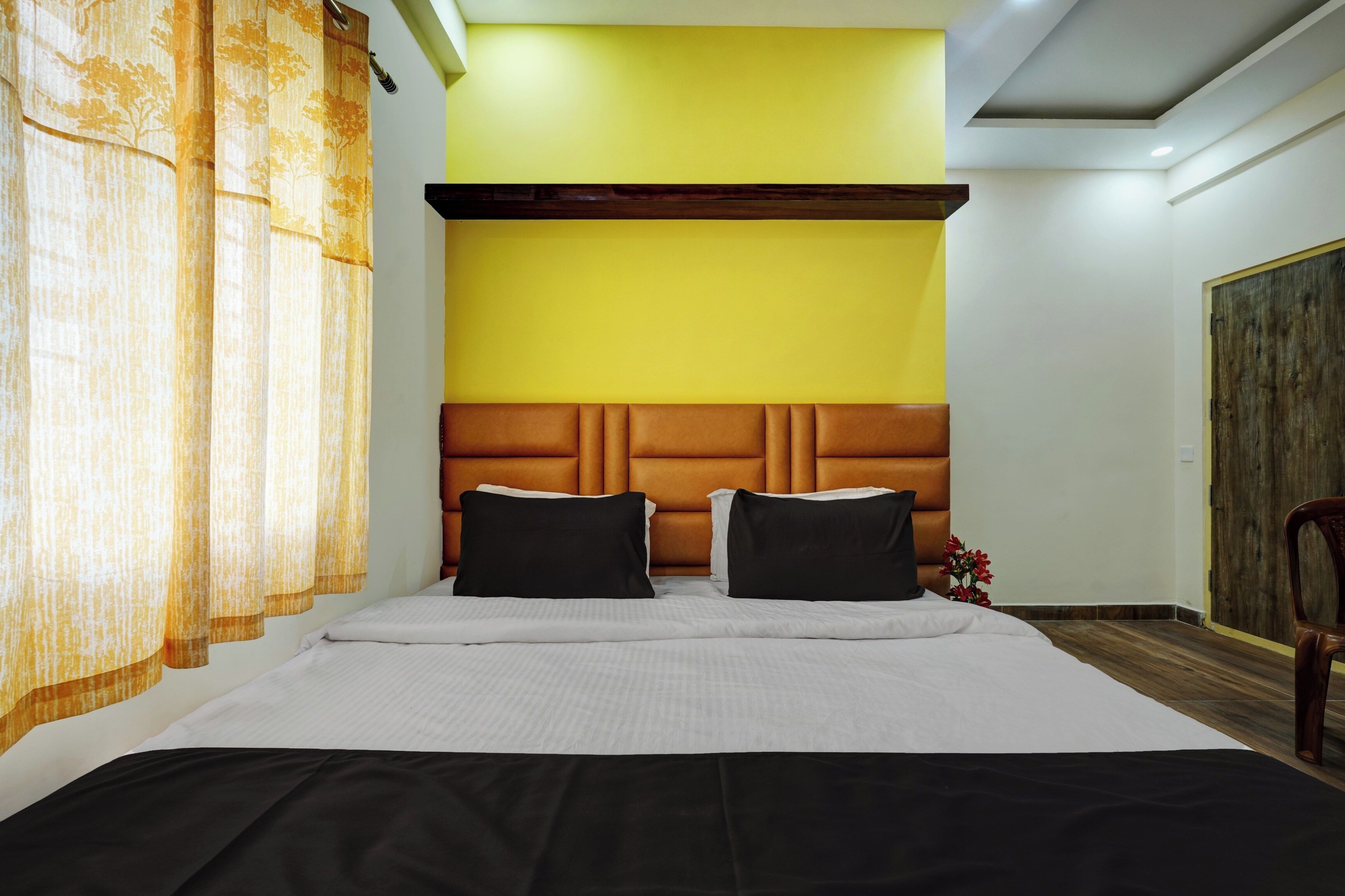 A hotel room with a large bed, a wooden headboard, and a yellow accent wall.