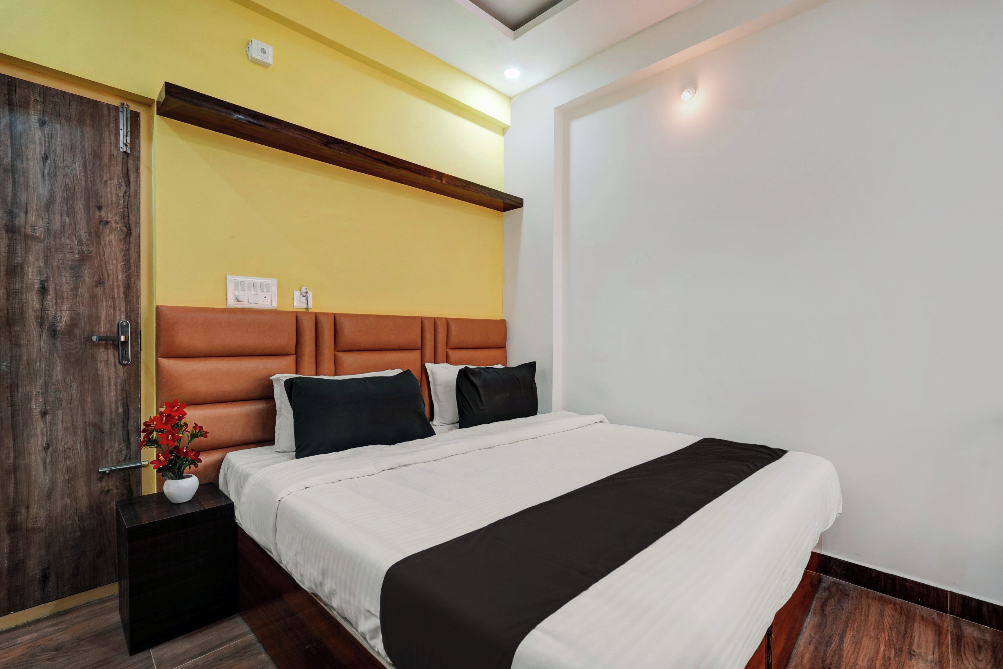 A hotel room with a bed, bedside tables, a nightstand, a wall-mounted light, and a door.