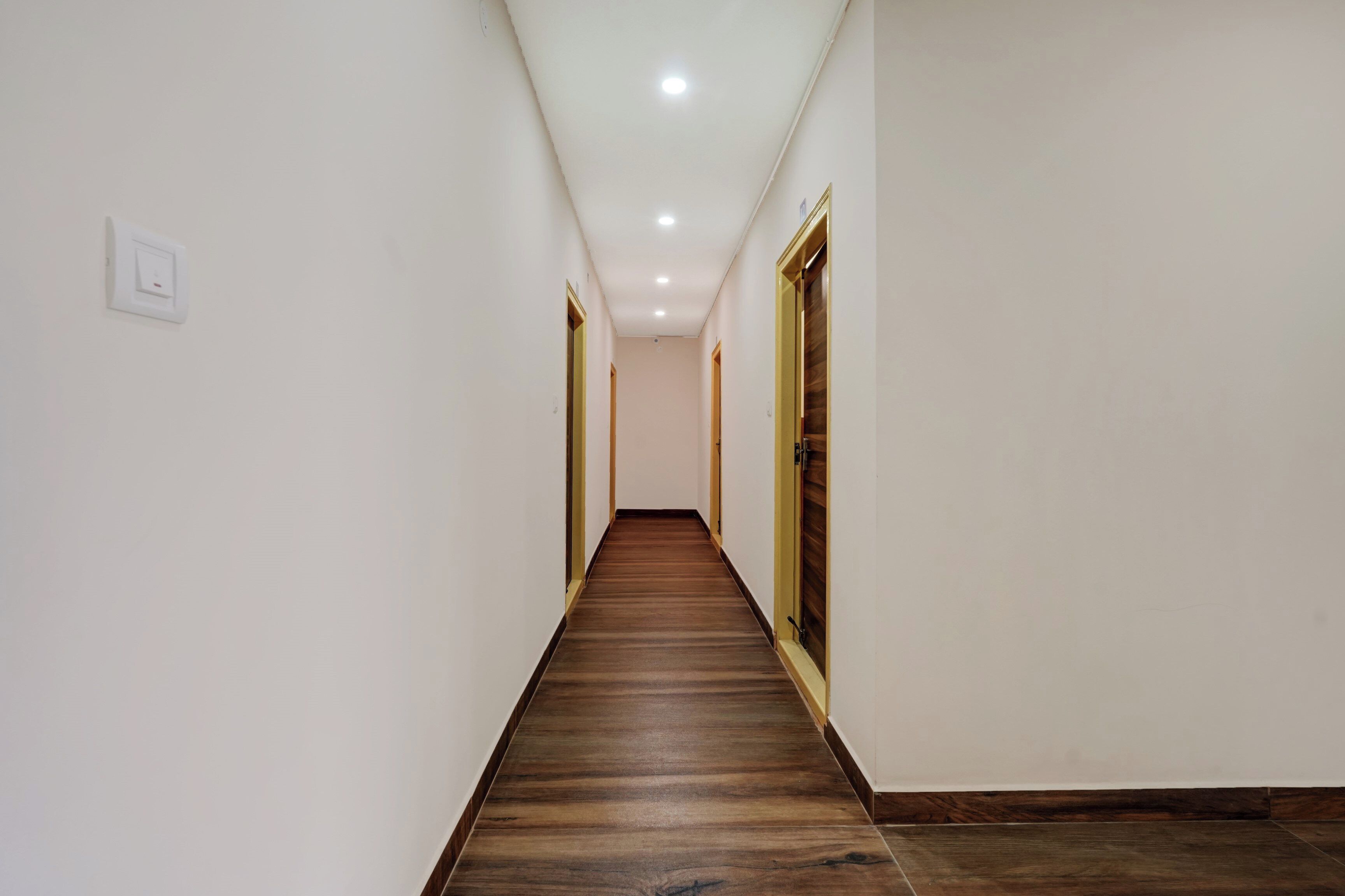 A corridor with a wooden floor, white walls, and doors on both sides.