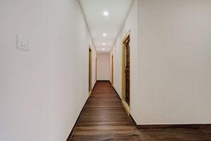 A corridor with a wooden floor, white walls, and doors on both sides. - Collection O Utsav Grand RR Nagar (Bangalore)
