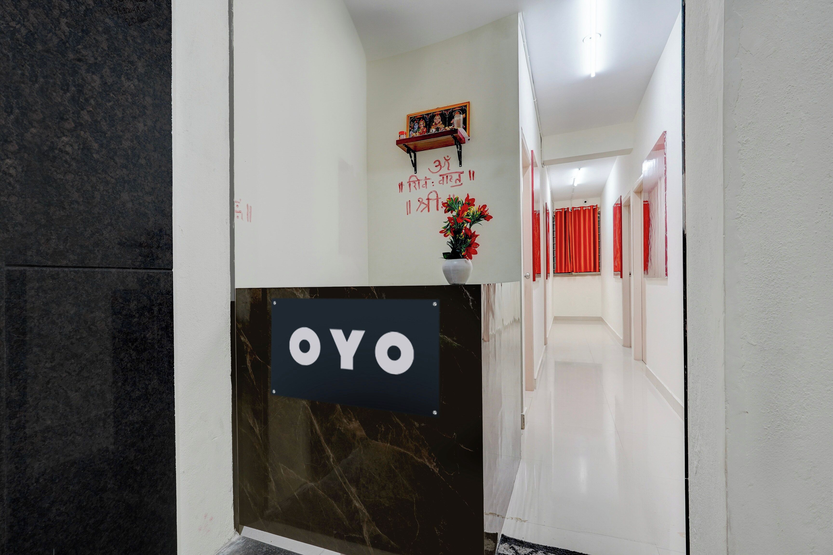 A reception area with a marble reception desk labeled 'OYO' and a wall with a religious painting and text.