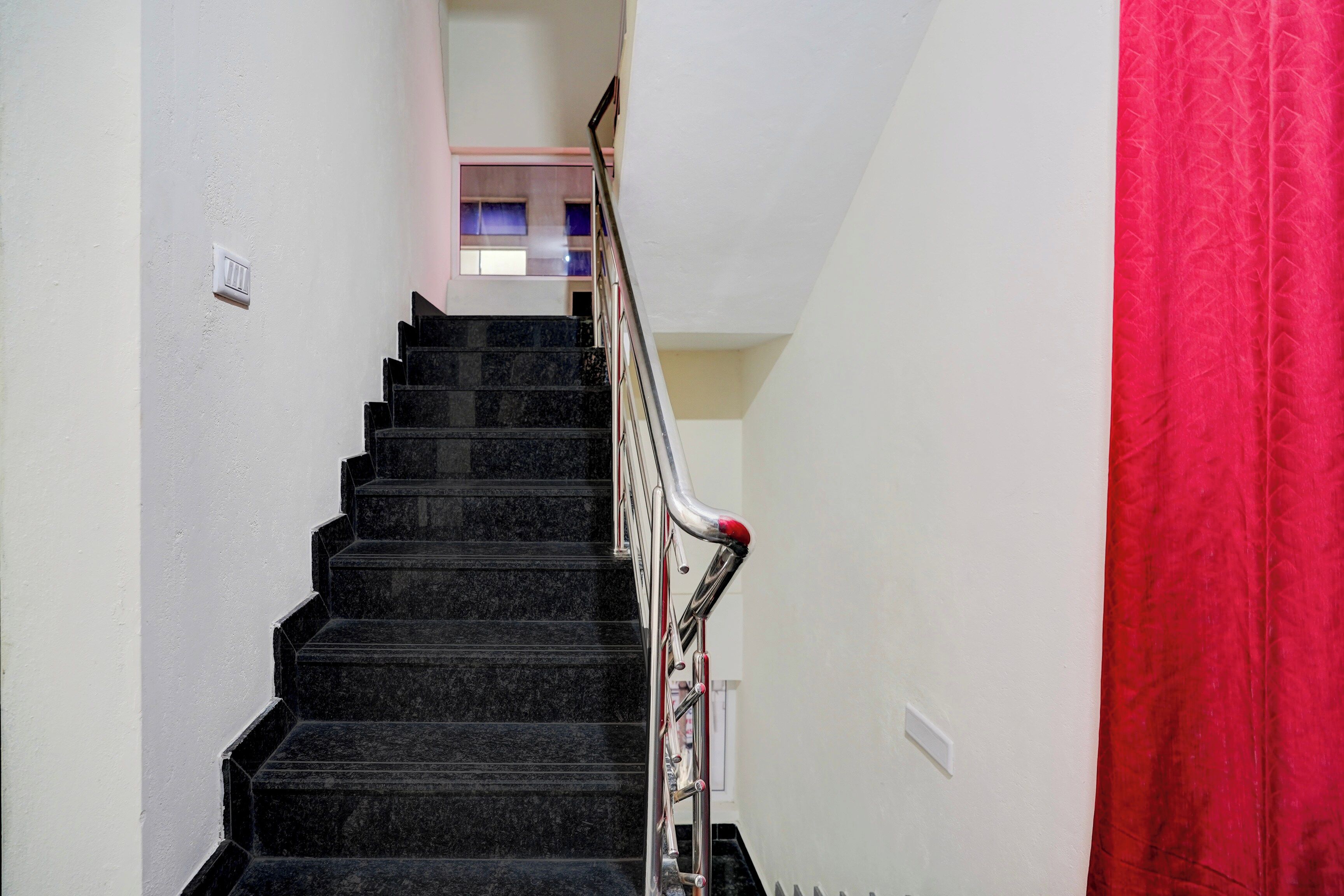 A staircase with a handrail, white walls, and a red curtain on the right.