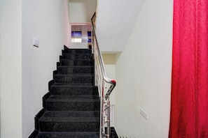 Una escalera con barandilla, paredes blancas y una cortina roja a la derecha.