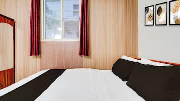 Un dormitorio con cama, ventana con cortinas y una pared decorada con cuadros.