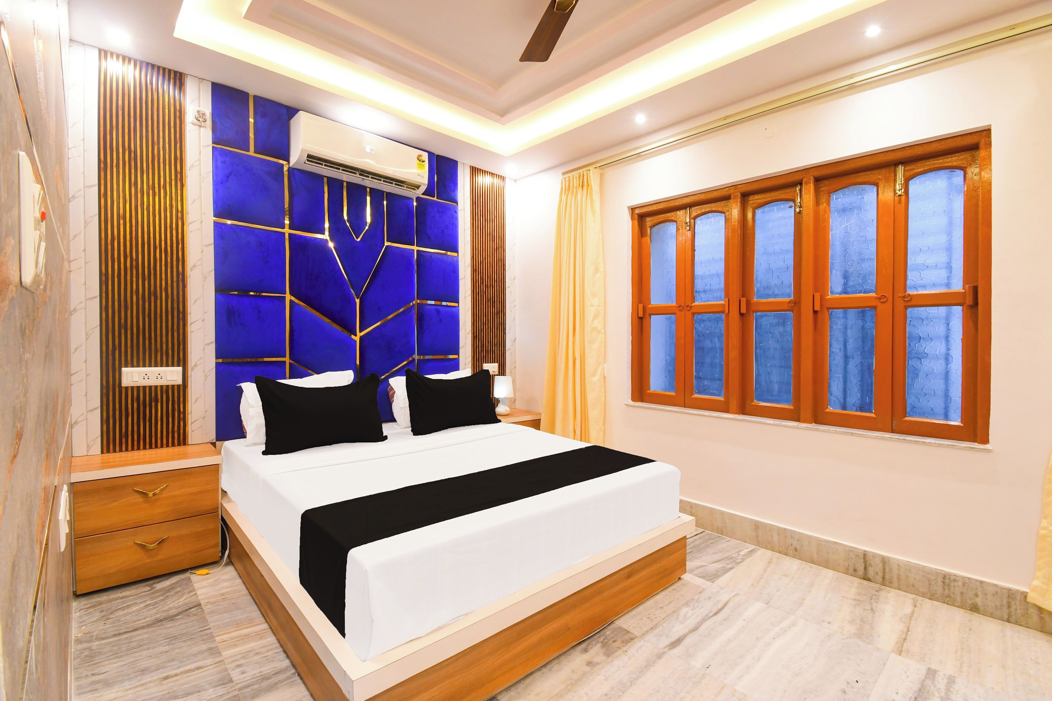 Un dormitorio moderno con una cama grande, una mesita de noche, un equipo de aire acondicionado y un ventanal con vidrio ornamental.