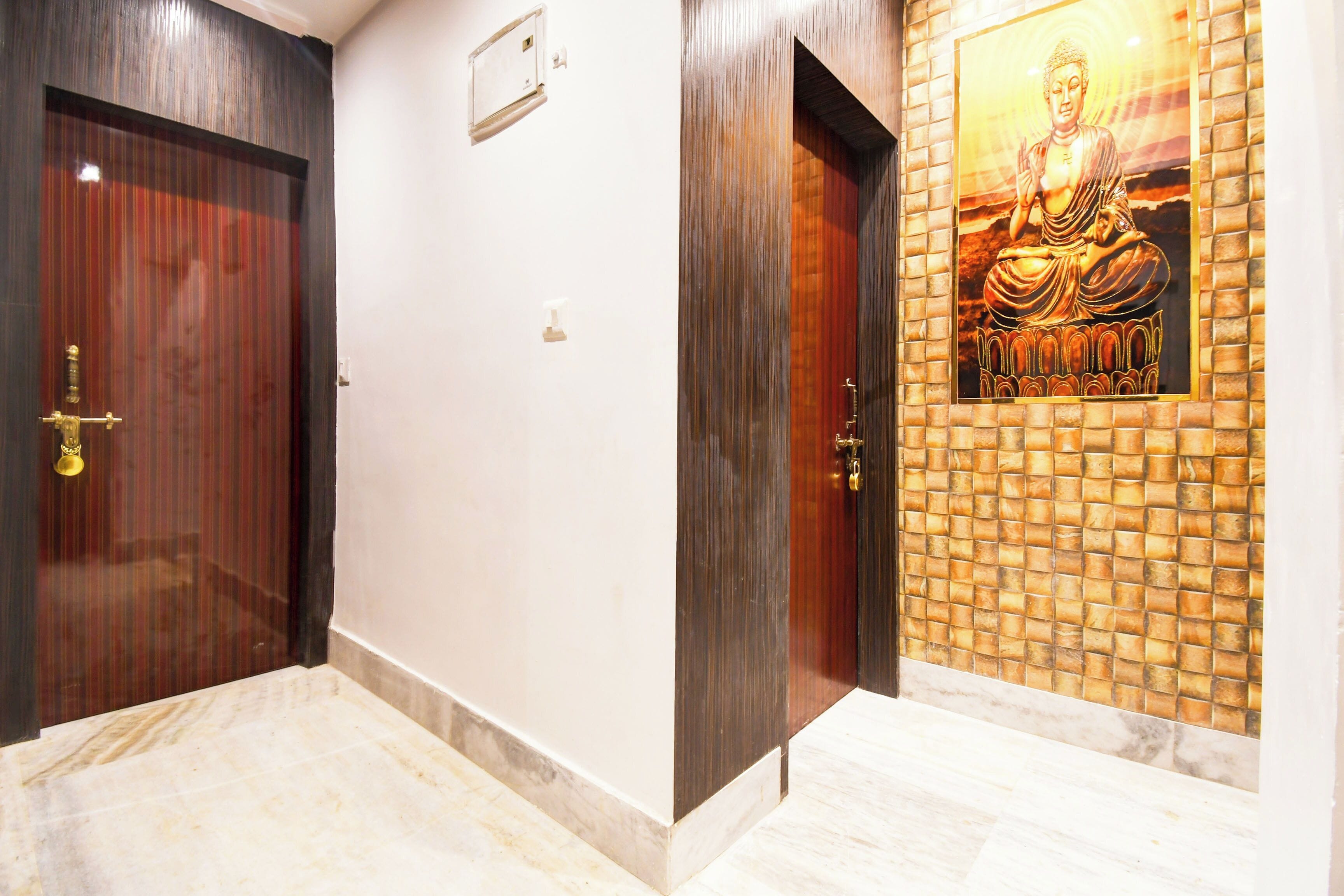 Un pasillo con dos puertas de madera, un muro con azulejos y una estatua de Buda, y un suelo de mármol.