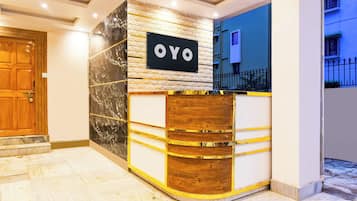 Una mesa de recepción con un letrero que dice 'OYO' y una pared de textura de piedra al fondo.