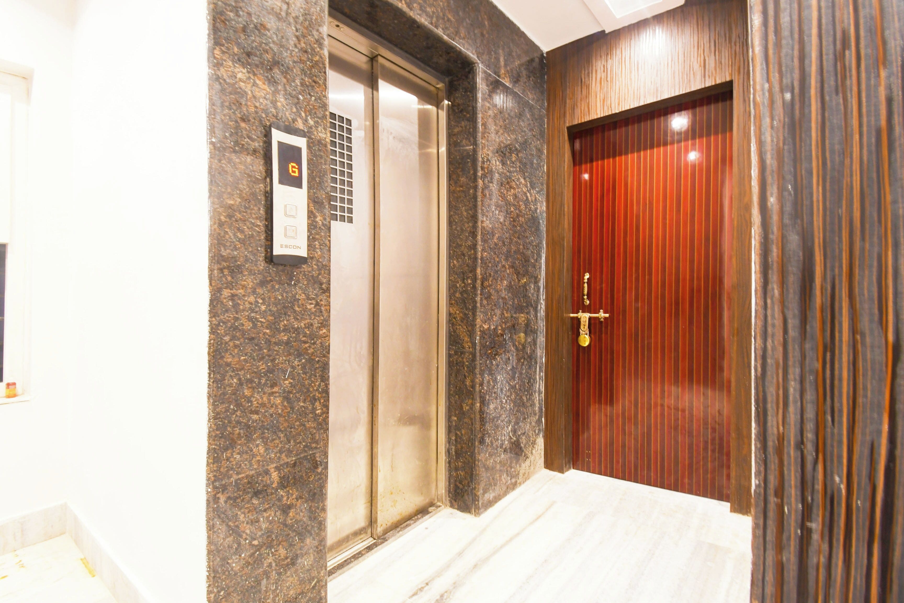A hotel entrance with a marble floor, a wooden door, and an elevator.