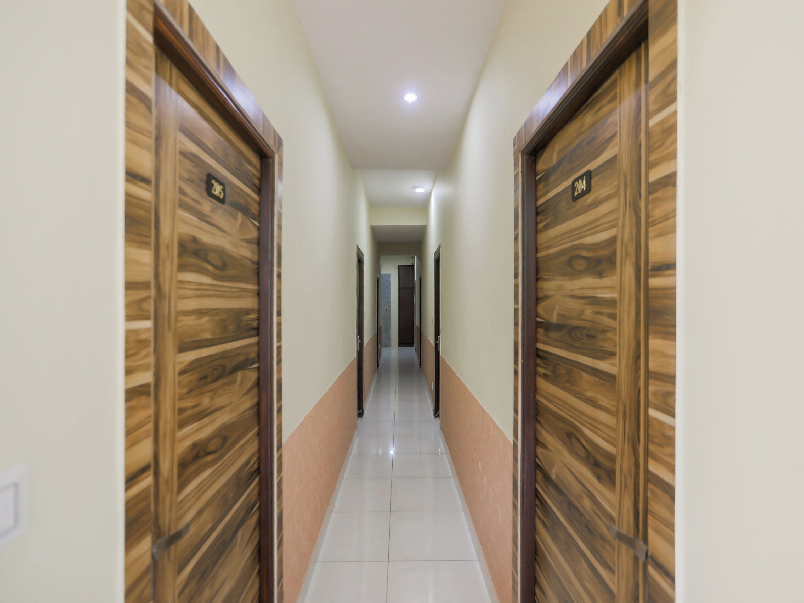 A corridor with wooden doors, white walls, and a tiled floor.