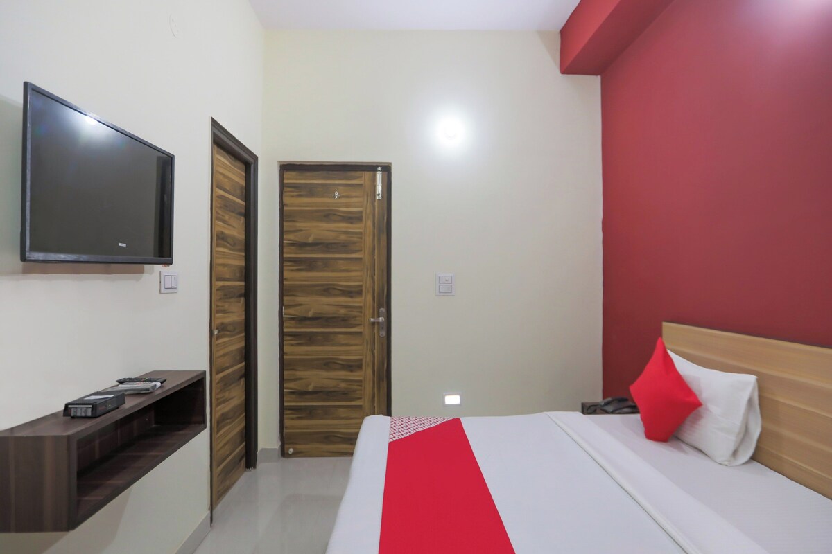 Habitación de hotel con una cama, un televisor montado en la pared, una puerta de madera y una pared decorada en rojo.