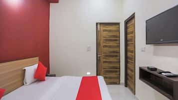 A hotel room with a bed, a TV mounted on the wall, a wooden door, and a small table with a remote control.