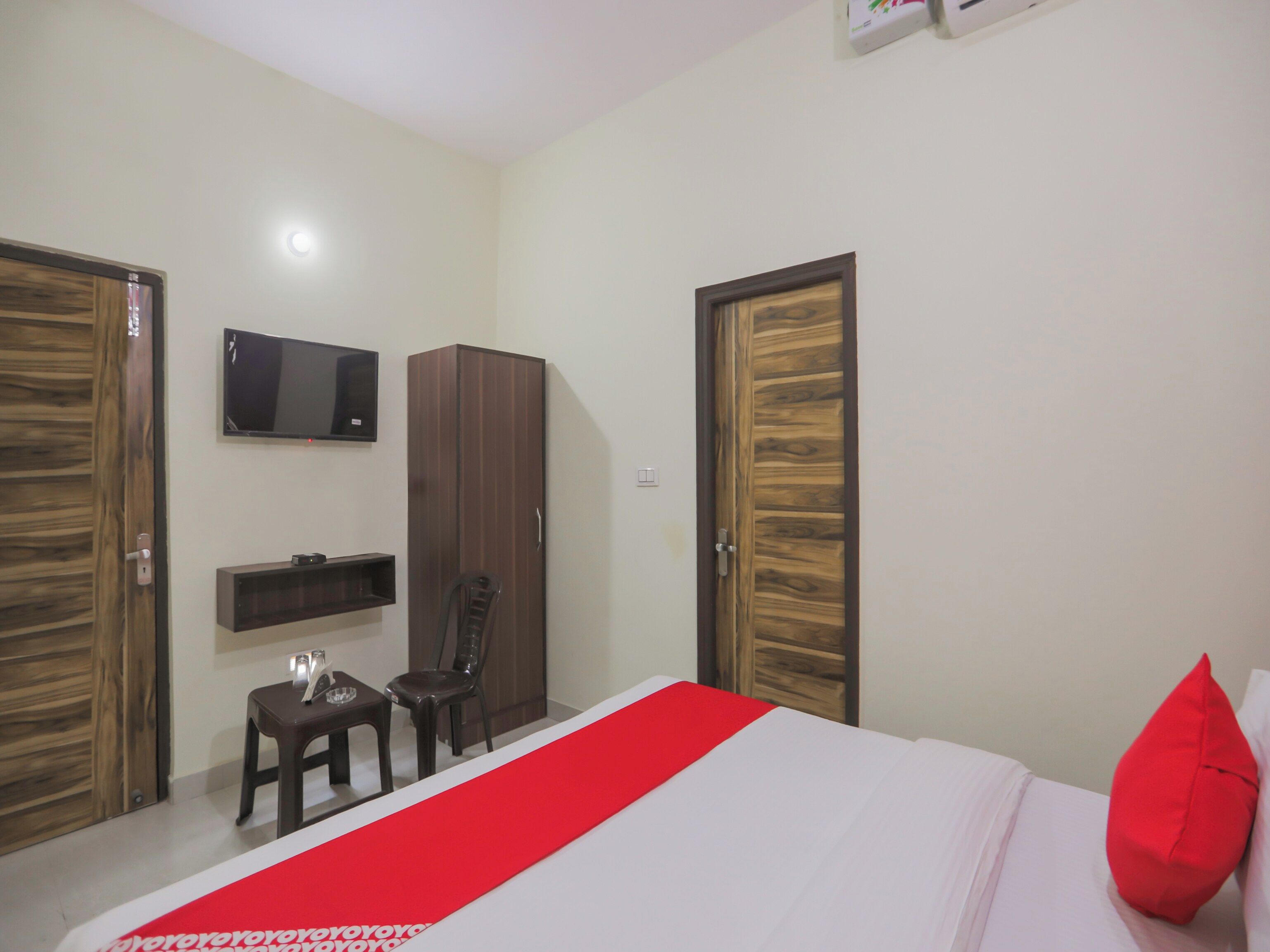 Un dormitorio con cama, televisor montado en la pared, armario y una silla.