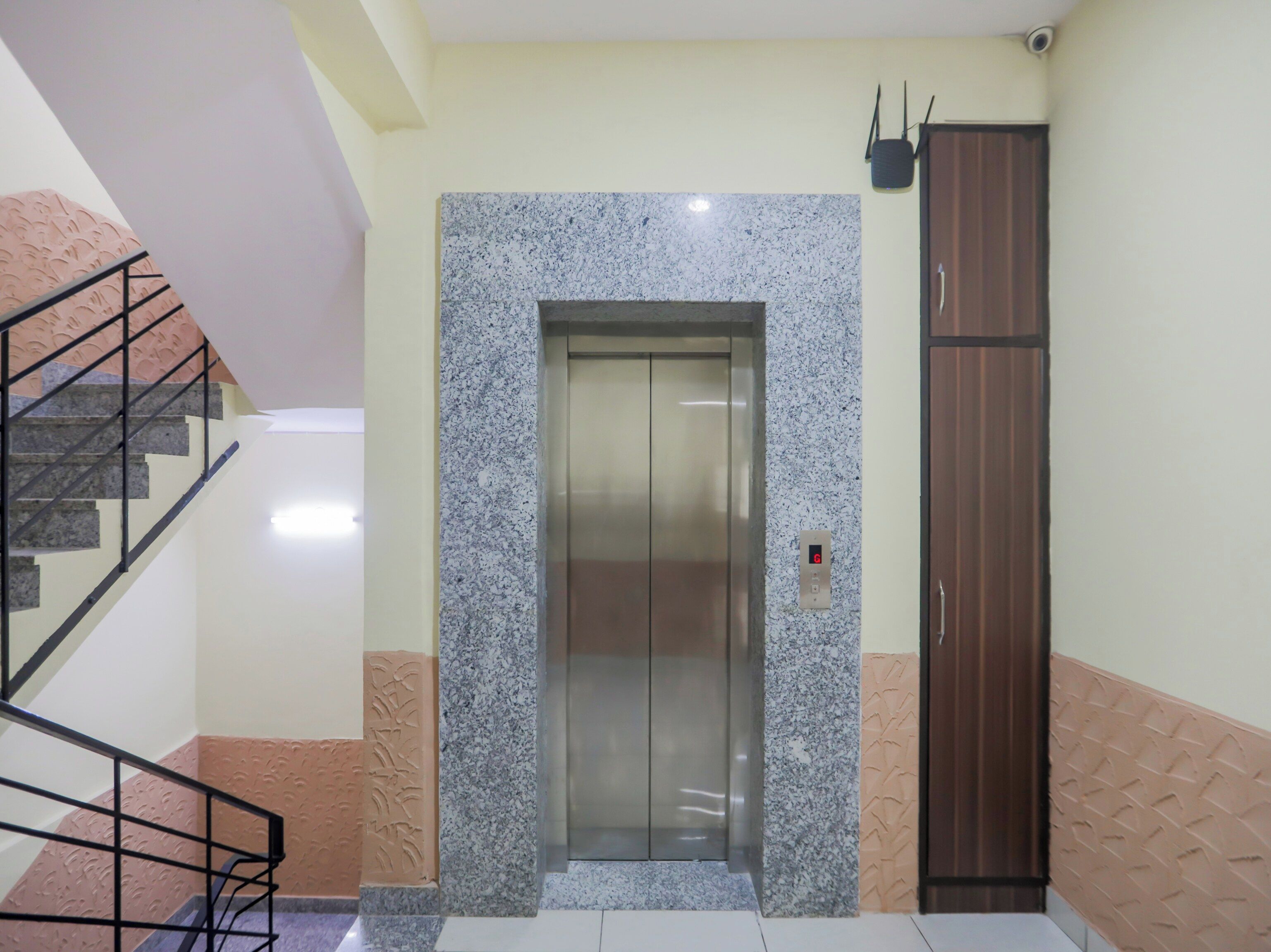 Un ascensor con pantalla digital, una escalera con barandillas de metal y un armario marrón.