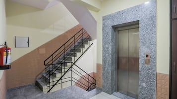 A staircase with a metal railing, an elevator, and a fire extinguisher on the wall.
