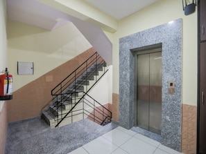 Una escalera con barandilla de metal, un ascensor y un extintor en la pared.