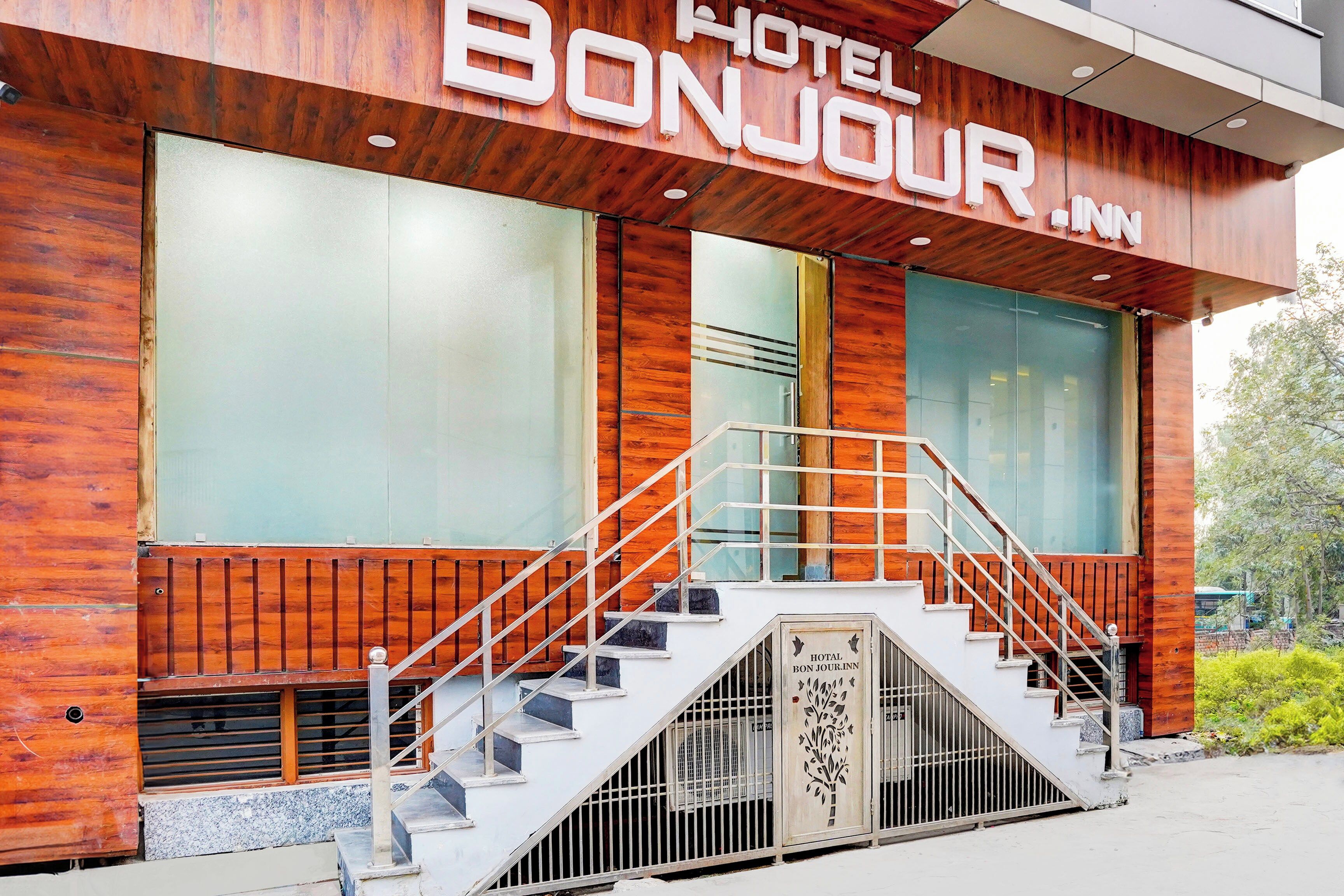 A hotel named 'HOTEL BONJOUR.INN' with a wooden facade, large windows, and a staircase leading to the entrance.