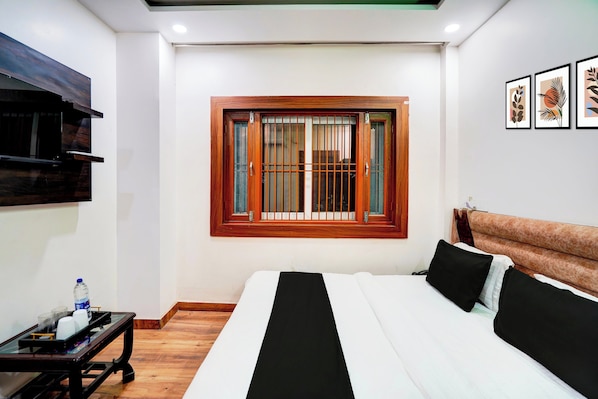 A hotel room with a bed, a small table, a window with bars, and framed artwork on the wall.