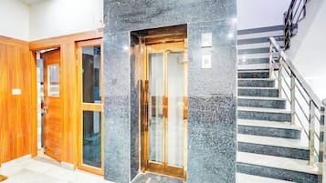 A hotel entrance with a wooden door, a glass door, and a staircase with metal railings.