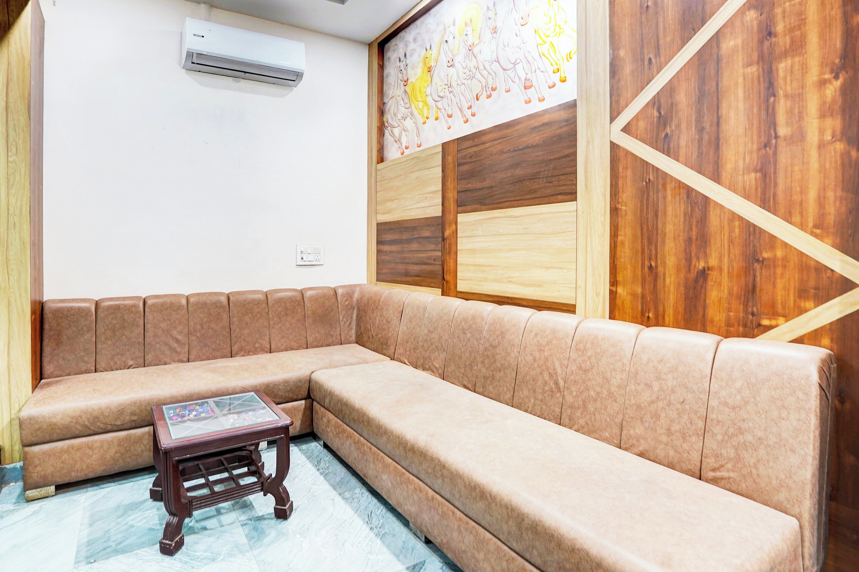 A room with a brown sectional sofa, a small wooden table, and a wall-mounted air conditioner.